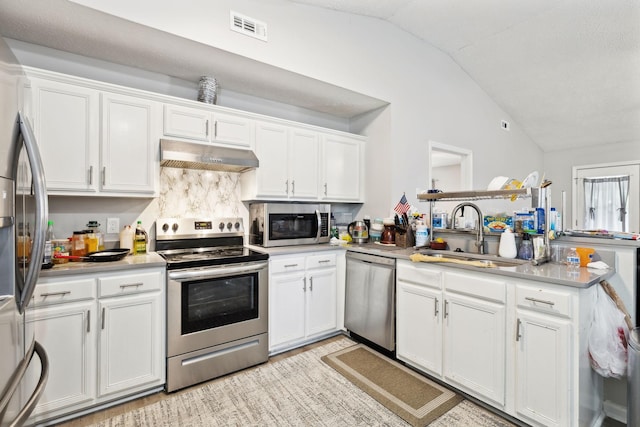 kitchen featuring appliances with stainless steel finishes, lofted ceiling, under cabinet range hood, a sink, and white cabinetry