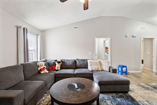 living room featuring wood finished floors, vaulted ceiling, a ceiling fan, baseboards, and a textured ceiling