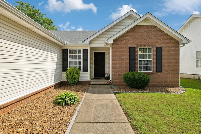 entrance to property with a lawn, brick siding, and a shingled roof