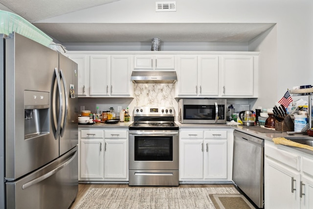 kitchen with stainless steel appliances, under cabinet range hood, white cabinetry, and light wood-style floors
