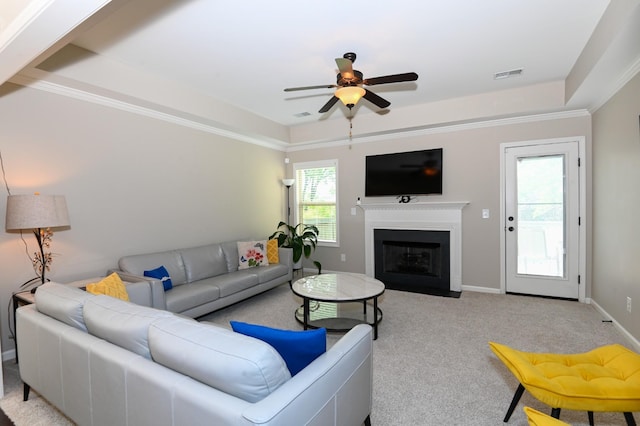 carpeted living room featuring visible vents, a fireplace with flush hearth, baseboards, a tray ceiling, and a ceiling fan