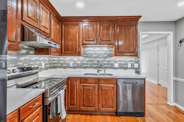 kitchen featuring decorative backsplash, light countertops, under cabinet range hood, a sink, and appliances with stainless steel finishes