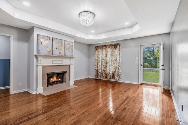 unfurnished living room with wood-type flooring, a chandelier, a tiled fireplace, baseboards, and a tray ceiling