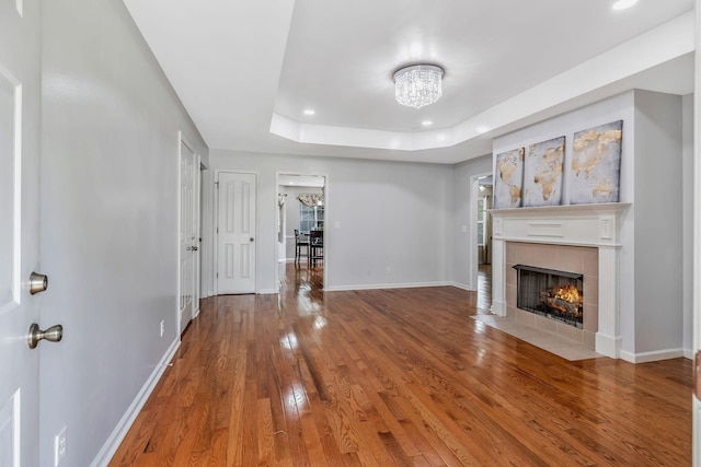 unfurnished living room featuring a tiled fireplace, baseboards, hardwood / wood-style floors, and a chandelier