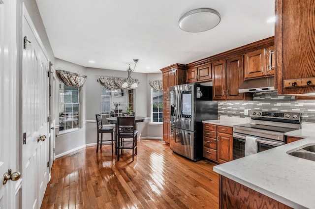 kitchen featuring appliances with stainless steel finishes, under cabinet range hood, hardwood / wood-style flooring, and tasteful backsplash