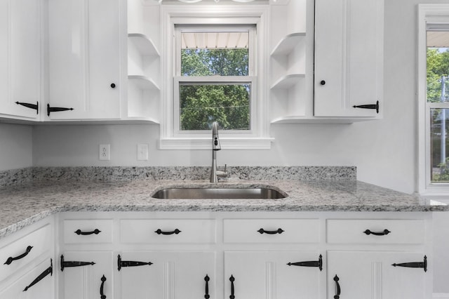 kitchen featuring a sink, white cabinets, open shelves, and light stone countertops