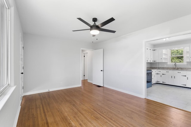 unfurnished living room featuring light wood-type flooring, a ceiling fan, a sink, and baseboards