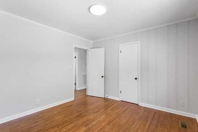 unfurnished bedroom with baseboards, ornamental molding, wood finished floors, and visible vents