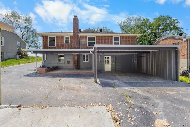 back of property featuring central AC, aphalt driveway, brick siding, a chimney, and a carport