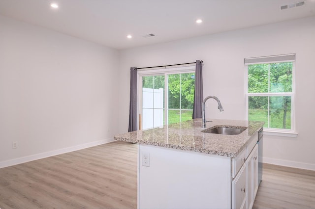 kitchen with white cabinets, a sink, visible vents, light wood finished floors, and an island with sink