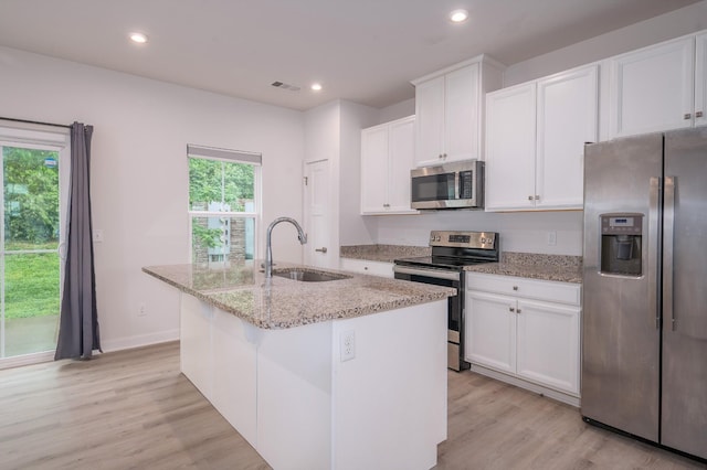 kitchen with white cabinetry, a sink, stainless steel appliances, light wood-type flooring, and a center island with sink