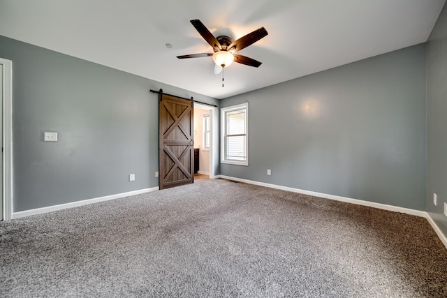carpeted empty room with ceiling fan, a barn door, and baseboards