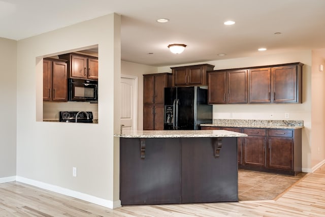 kitchen featuring light stone counters, black appliances, light wood-type flooring, and dark brown cabinets