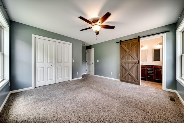 unfurnished bedroom with a closet, carpet flooring, a barn door, and visible vents