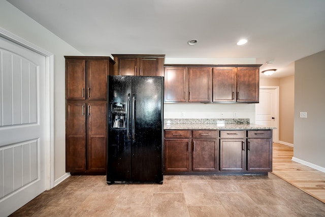 kitchen featuring dark brown cabinets, light stone countertops, black refrigerator with ice dispenser, recessed lighting, and baseboards