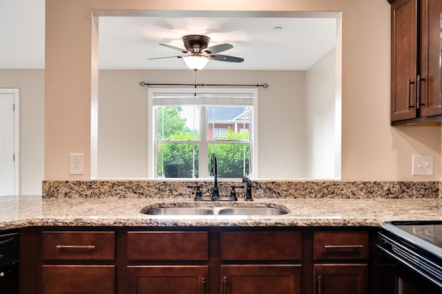 kitchen with a sink, dark brown cabinetry, a ceiling fan, and light stone countertops