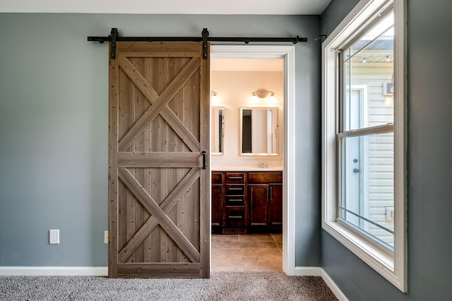 interior space featuring baseboards, light carpet, a wealth of natural light, and a barn door