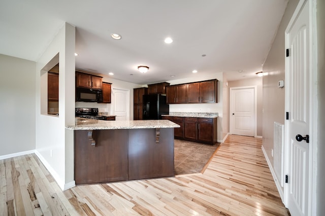 kitchen featuring a peninsula, light stone counters, light wood finished floors, and black appliances