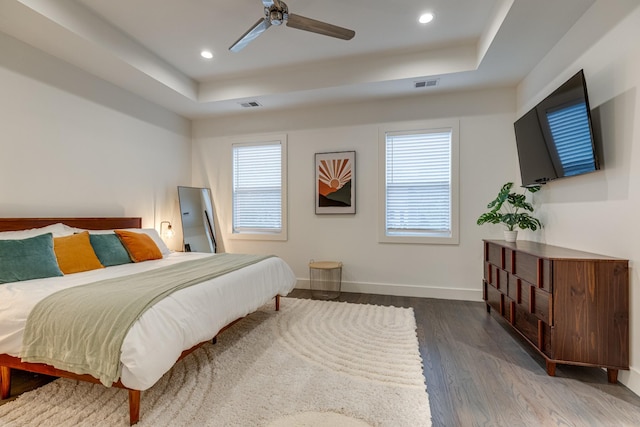bedroom featuring wood finished floors, visible vents, a raised ceiling, and baseboards
