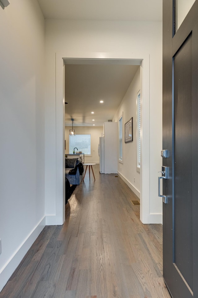 hallway featuring wood finished floors, recessed lighting, and baseboards
