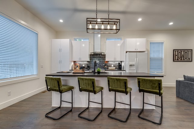 kitchen featuring white refrigerator with ice dispenser, a breakfast bar area, extractor fan, dark countertops, and white cabinetry