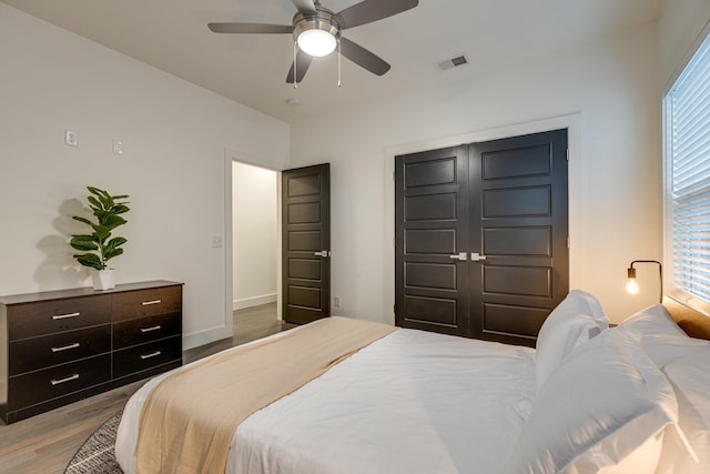 bedroom with a closet, a ceiling fan, visible vents, baseboards, and wood finished floors