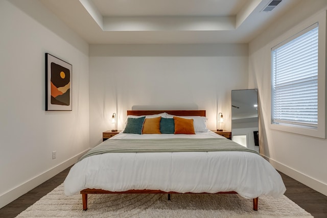 bedroom with dark wood-type flooring, a raised ceiling, visible vents, and baseboards