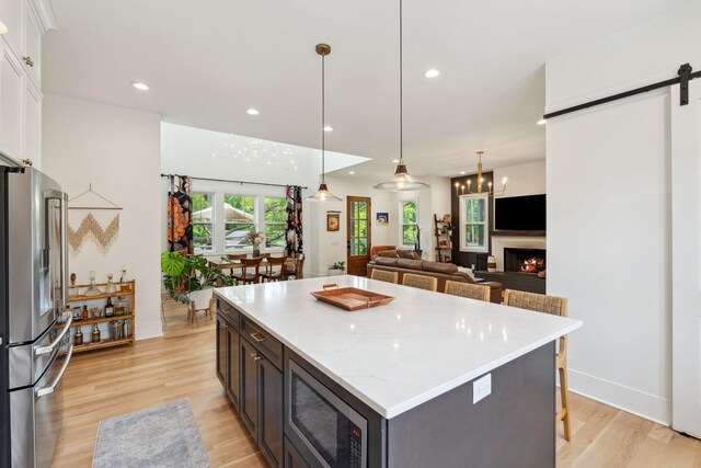 kitchen featuring white cabinets, a barn door, light wood-style flooring, a center island, and stainless steel appliances