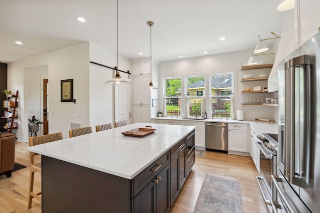 kitchen with a breakfast bar area, open shelves, premium appliances, recessed lighting, and white cabinetry