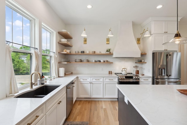 kitchen featuring open shelves, appliances with stainless steel finishes, a sink, light wood-style flooring, and premium range hood