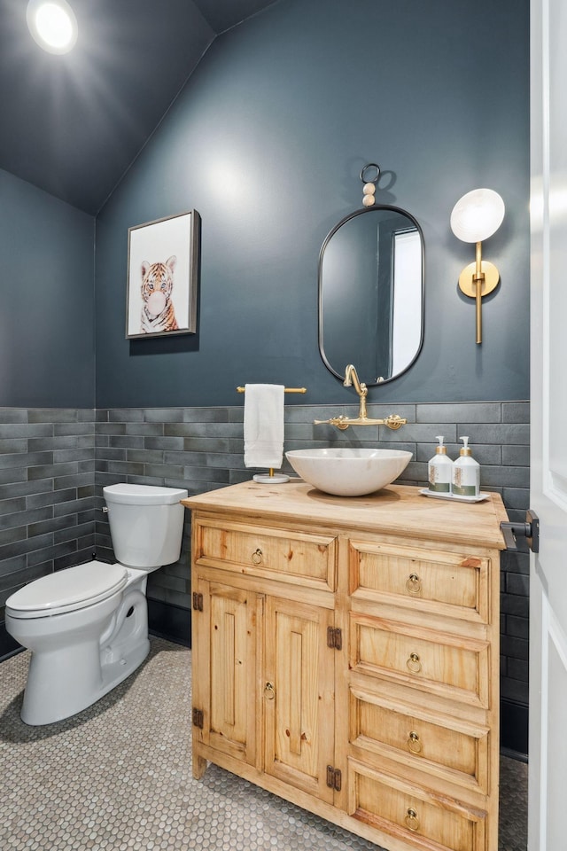 bathroom with vanity, lofted ceiling, toilet, tile walls, and a wainscoted wall