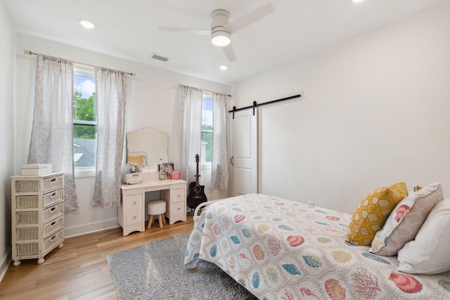 bedroom featuring visible vents, a barn door, baseboards, light wood-style floors, and recessed lighting