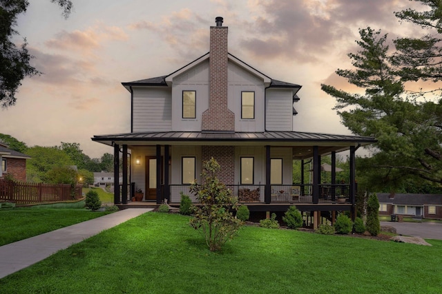 view of front of home with covered porch, a standing seam roof, a chimney, metal roof, and a yard