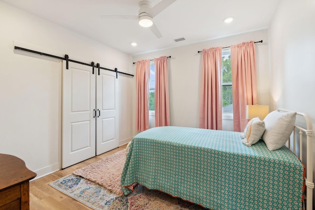 bedroom featuring ceiling fan, a barn door, baseboards, light wood-type flooring, and visible vents