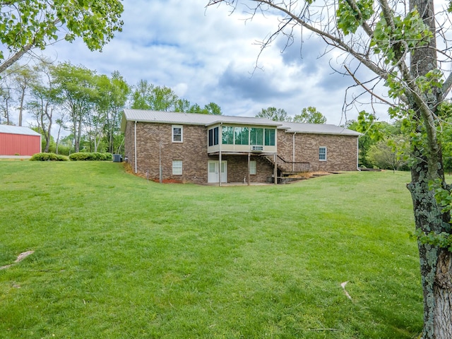 back of house featuring a sunroom, stairway, metal roof, a lawn, and brick siding
