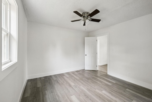 empty room with a ceiling fan, wood finished floors, a textured ceiling, and baseboards