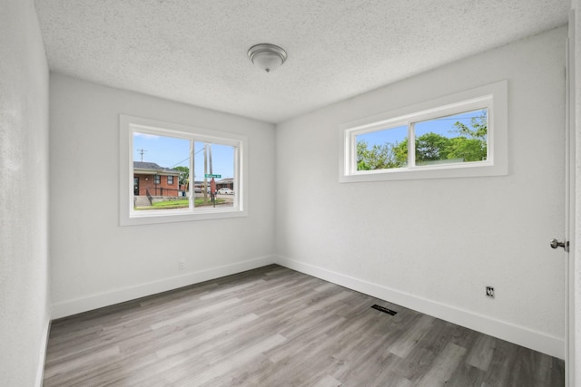 spare room with baseboards, visible vents, wood finished floors, and a textured ceiling