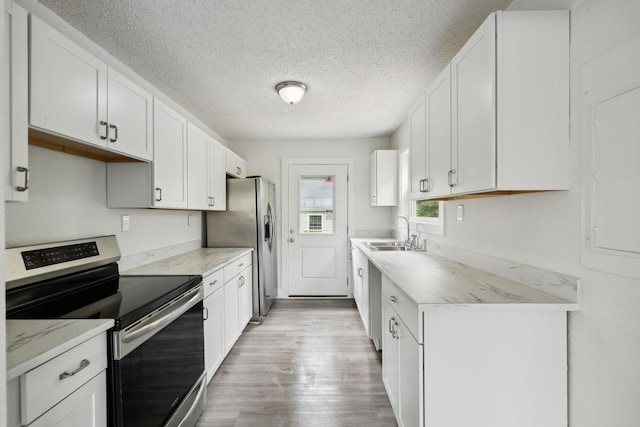 kitchen with wood finished floors, appliances with stainless steel finishes, a sink, white cabinetry, and a textured ceiling