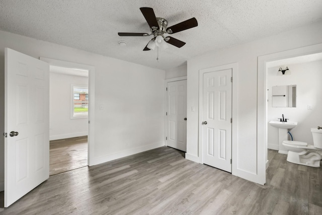unfurnished bedroom featuring a textured ceiling, connected bathroom, ceiling fan, baseboards, and wood finished floors