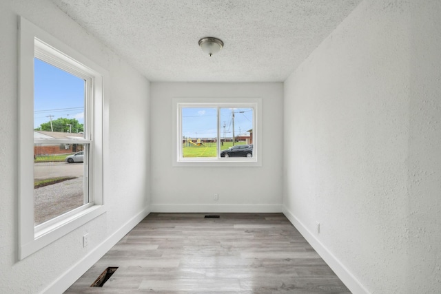 unfurnished room with baseboards, wood finished floors, a wealth of natural light, and a textured ceiling