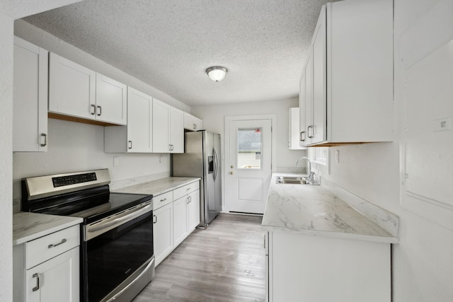 kitchen featuring light wood finished floors, a sink, light countertops, a textured ceiling, and appliances with stainless steel finishes
