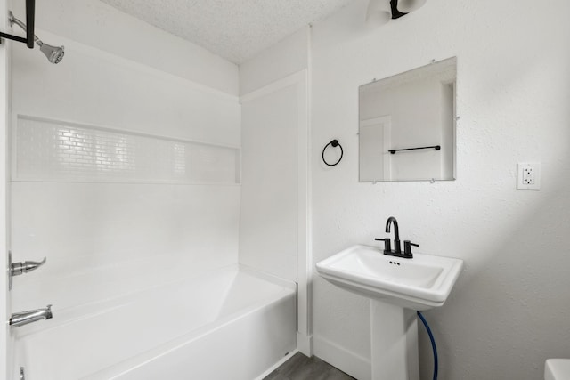 bathroom with a textured ceiling, baseboards, wood finished floors, and  shower combination