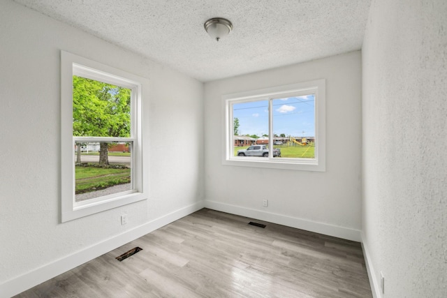unfurnished room with baseboards, visible vents, wood finished floors, and a textured ceiling