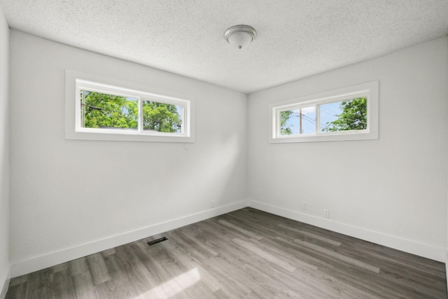 unfurnished room featuring a textured ceiling, visible vents, wood finished floors, and baseboards