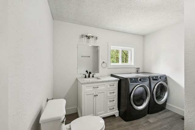 washroom with dark wood-style floors, a sink, separate washer and dryer, baseboards, and a textured ceiling