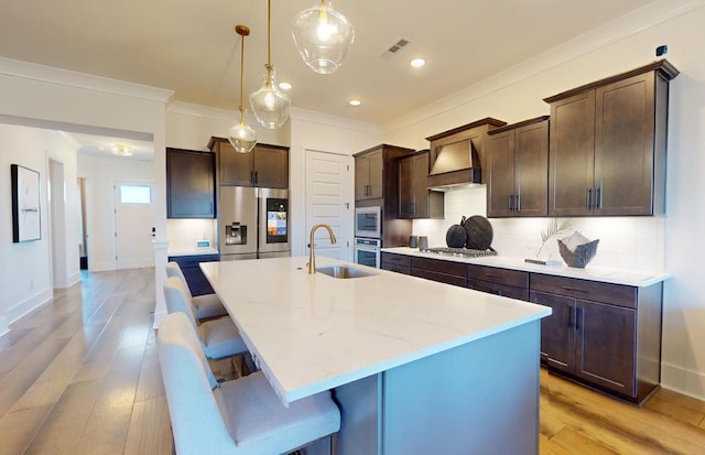 kitchen featuring appliances with stainless steel finishes, dark brown cabinets, ornamental molding, a sink, and premium range hood