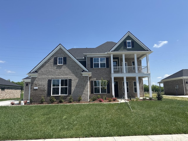 greek revival inspired property featuring brick siding, a front lawn, and a balcony