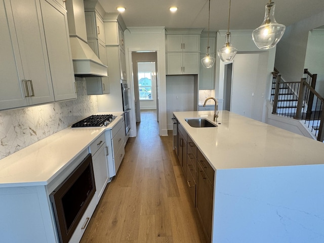 kitchen featuring stainless steel appliances, backsplash, light wood finished floors, and a sink