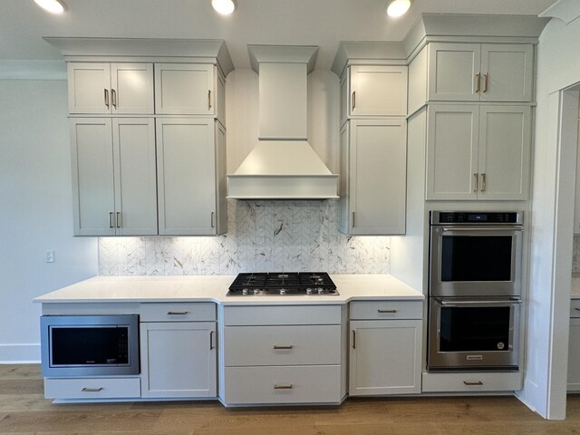 kitchen with tasteful backsplash, custom exhaust hood, stainless steel appliances, and wood finished floors