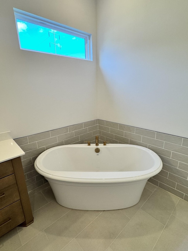 full bath featuring a freestanding tub, vanity, tile patterned floors, and tile walls